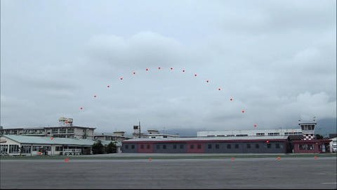 Auf einem schwarz-weiß Bild ist die rote Flugkurve eines Balles eingezeichnet.