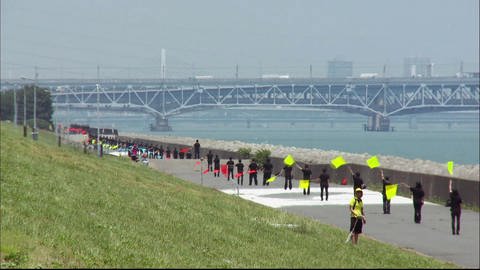 Viele schwarzgekleidete Personen stehen an einer Flußpromenade und schwenken bunte Fahnen.