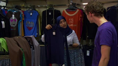 Ein junger Mann ist in einem Modegeschäft und wird von einer jungen Frau mit Hijab beraten.
