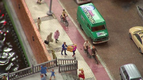 Aufnahme von oben: eine Miniaturstraße mit vielen Menschen und einem grünen Bus mit dem Schriftzug "2 durch Deutschland"