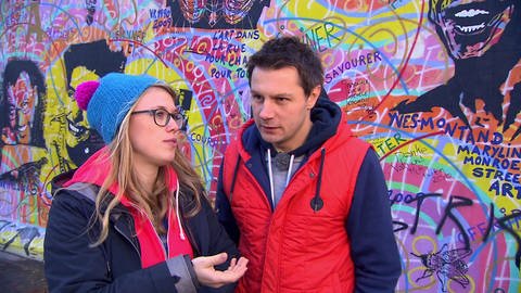 Ein Mann und eine Frau stehen vor einer mit Graffiti besprühten Wand. 