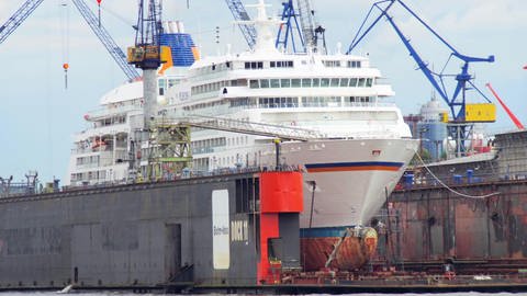 Ein großes Schiff liegt in einem Schiffsdock und wird mit verschiedenen Geräten gereinigt und repariert.