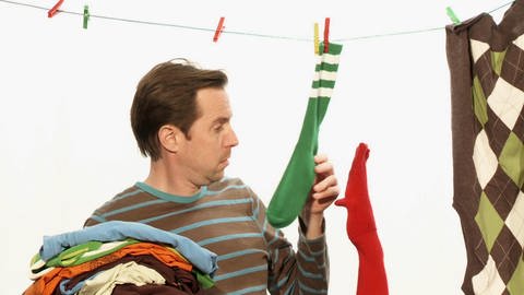 Ein Mann und eine rote Strumpfhandpuppe hängen Wäsche ab.