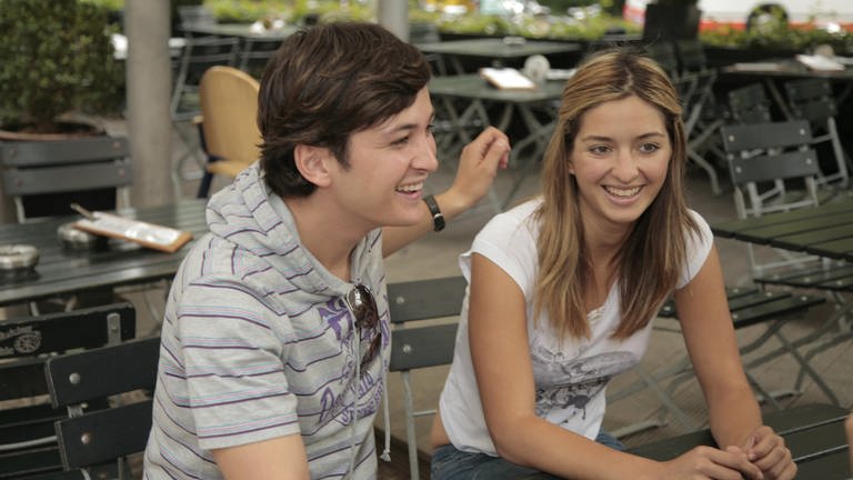 Ein junger Mann und eine junge Frau sitzten nebeneinander und lächeln. 