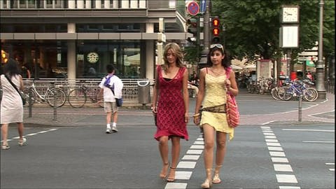 Zwei junge Frauen in bunten Kleidern laufen in Köln über die Straße.