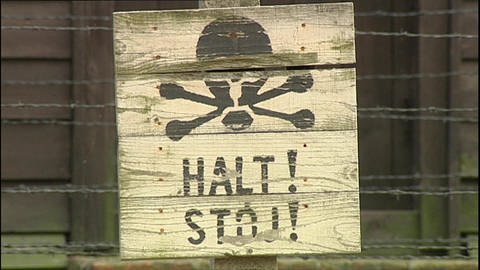 Ein Schild mit Totenkopf und dem Schriftzug "Halt! Stop!" vor einem Stacheldrahtzaun.