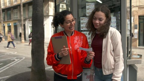Zwei junge Frauen stehen vor einem Kiosk und schauen sich einen Lottoschein an. (Foto: WDR)