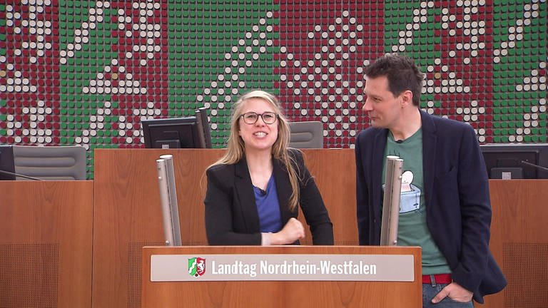 Ein Mann und eine Frau stehen im Landtag von Nordrhein-Westfalen an einem Pult.