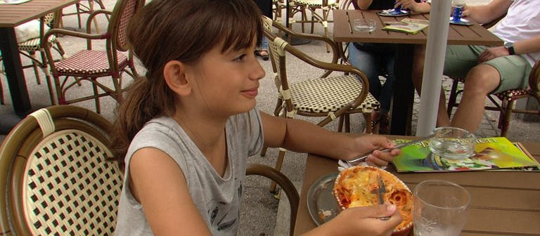 Ein Mädchen sitzt an einem Tisch im Biergarten und isst Lasagne.  (Foto: WDR)