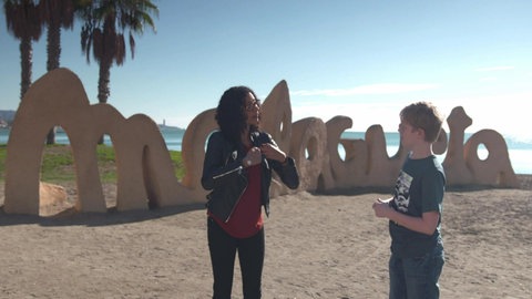 Ein Junge und eine Frau stehen am Strand unter Palmen und reden miteinander.