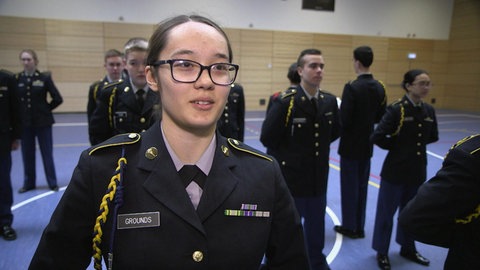 Ein Mädchen und andere junge Menschen stehen in Uniform in einer Turnhalle.