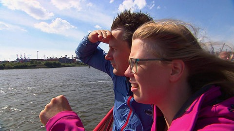 Zwei Personen stehen am Wasser und schauen in die Ferne.