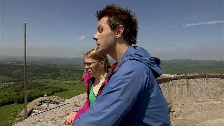 Ein Mann und eine Frau stehen auf einer Aussichtsplattform und schauen ins Tal hinab.
