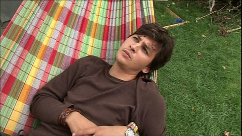 Ein junger Mann liegt in einer Hängematte und schaut nachdenklich in den Himmel.