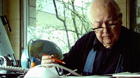 Schriftsteller Friedrich Dürrenmatt sitzt mit einem Stift in der Hand an einem Schreibtisch.