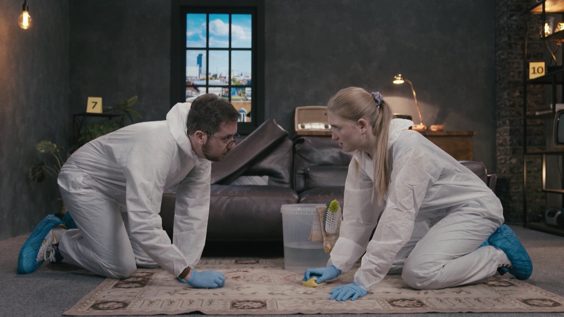 Zwei Personen in Schutzanzügen knien auf einem Teppich und reinigen ihn mit Schwämmen.