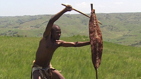 Ein Kämpfer mit Schutzschild in der Hand schwingt seinen Stock