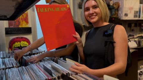 Lily hält in einem Plattenladen eine LP in die Kamera