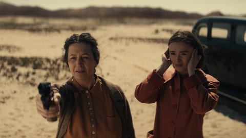 Spielszene: Golda Meir will ihr Land Israel verteidigen. Sie macht Schießübungen in der Wüste; ihre Tochter steht neben ihr und hält sich die Ohren zu.