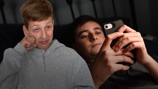 Trauriger Schüler im Vordergrund, im Hintergrund ein Kind am Smartphone