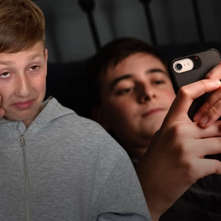 Trauriger Schüler im Vordergrund, im Hintergrund ein Kind am Smartphone