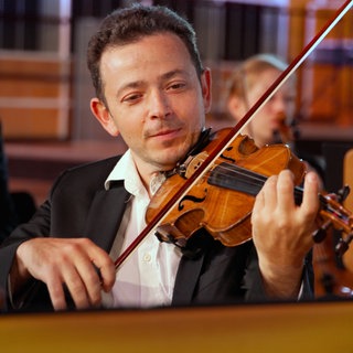 Ein Mann spielt Violine, im Hintergrund weitere Mitglieder der Streichergruppe.
