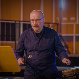 Ein Schlagwerker des Orchesters mit spannungsvollem Gesichtsausdruck kurz vor seinem Einsatz an einer Trommel.