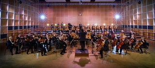 Ein Sinfonieorchester spielt in einem Probensaal. Jede Instrumentengruppe trägt zum Gesamtklang des Orchesters bei.