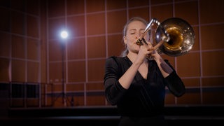 Eine Frau spielt Posaune. Dieses Instrument gehört zur Gruppe der Blechbläser.