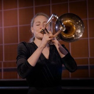 Eine Frau spielt Posaune. Dieses Instrument gehört zur Gruppe der Blechbläser.