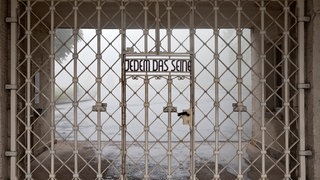 Der Schriftzug „Jedem das Seine“ auf dem weißen Gitter des Eingangs zum Konzentrationslagers Buchenwald. Der Ausdruck hat seit dem Nationalsozialismus eine negative Bedeutung.