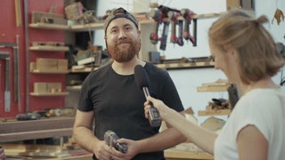 Stefanie mit Mikrofon in der Hand befragt eine Schreiner mit Akkuschrauber in der Hand