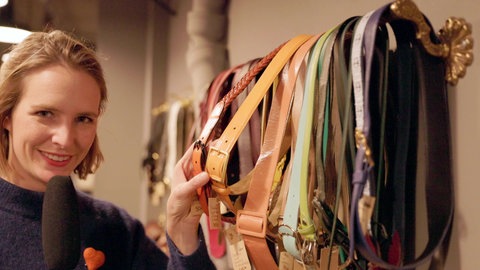 Stefanie mit Mikrofon in der Hand an eienr Wand mit Gürteln