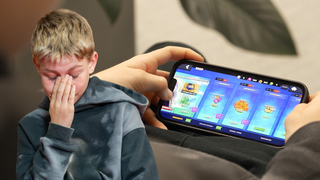 Im Vordergrund ein Junge, der frustriert nach unten schaut; im Hintergrund ein Handyspiel, bei dem gerade etwas gekauft wird