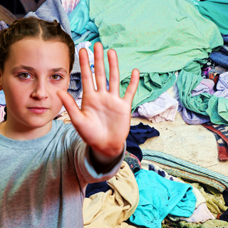 Im Vordergrund ein Mädchen in Abwehrhaltung, im Hintergrund ein großer Haufen bunter Wäsche