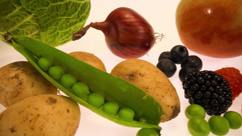 Nahaufnahme einer Erbsenschote mit anderem Gemüse und Obst. Welche Lebensmittel gehören zu einer gesunden Ernährung?