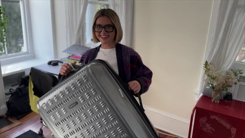 Lily hält einen Koffer in die Kamera