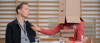 Moderator Jonas erzählt einer Person mit einem Karton über dem Kopf und einem Mikro eine Geschichte. Wie unterscheidet man das Imperfekt von anderen französischen Vergangenheitsformen?