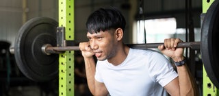 Junger Mann bei Kniebeugen mit einer Langhantel in einem Fitnessstudio