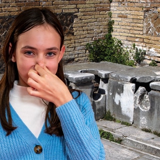 Im Hintergrund die Ruinen einer Toilettenanlage der alten Römer; im Vordergrund ein Mädchen, das sich die Nase zuhält