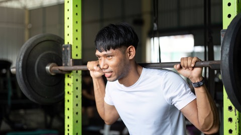 Junger Mann bei Kniebeugen mit einer Langhantel in einem Fitnessstudio