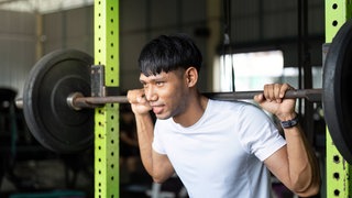 Junger Mann bei Kniebeugen mit einer Langhantel in einem Fitnessstudio