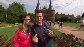 Eine Frau und ein Mann stehen in einem Park vor dem Holstentor, dem Stadttor Lübecks.