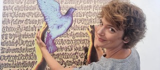 Moderatorin Lena Ganschow vor einer Tafel mit Friedenssymbolen