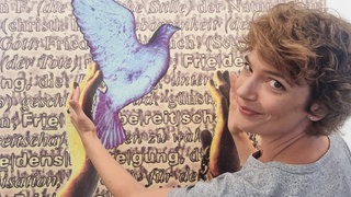 Moderatorin Lena Ganschow vor einer Tafel mit Friedenssymbolen