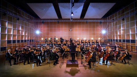Ein Sinfonieorchester spielt in einem Probensaal. Jede Instrumentengruppe trägt zum Gesamtklang des Orchesters bei.