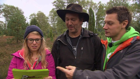 Zwei Männer und eine Frau stehen im Wald und lesen eine Karte.