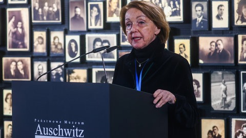 Die Holocaust-Überlebende Eva Umlauf bei einer Rede in der Gedenkstätte des Konzentrationslagers Auschwitz. Im Hintergrund eine Wand mit historischen Fotos.