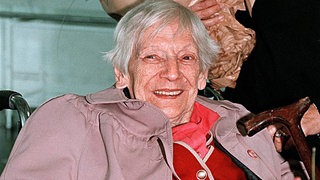 Emilie Schindler, die Witwe von Oskar Schindler, im Jahr 1999. Die grauhaarige Frau sitzt im Rollstuhl und hat Blumen auf dem Schoß.