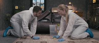 Zwei Personen in Schutzanzügen knien auf einem Teppich und reinigen ihn mit Schwämmen.